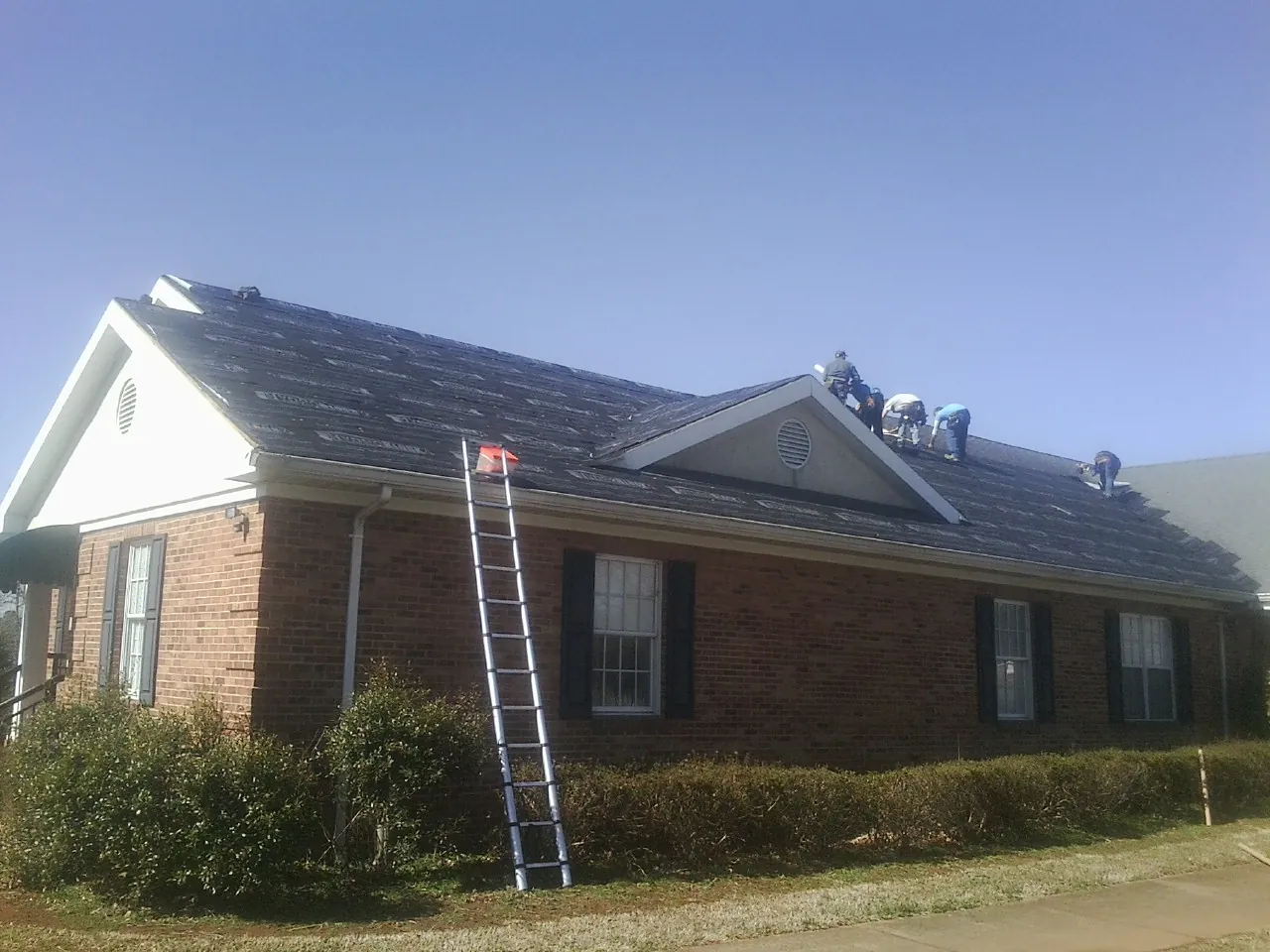 Crew tearing shingles off a brick ranch roof with a ladder set — Metal Roof Repair work by our crew in Marlboro