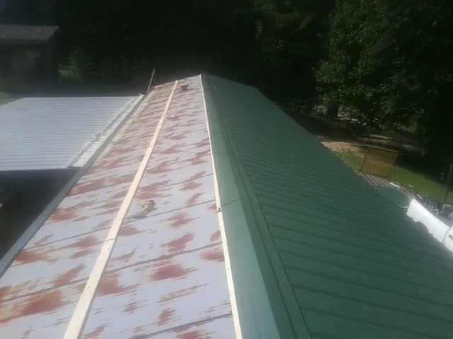 Old rusted panels beside newly installed green metal roofing — Wind Damage Roof Repair by Roofing Brothers in Marlboro