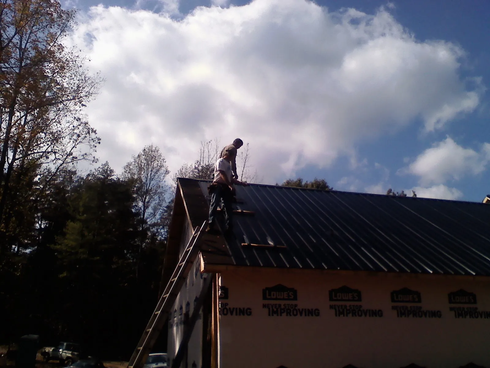Roofer fastening dark metal panels high against a cloudy sky in Marlboro