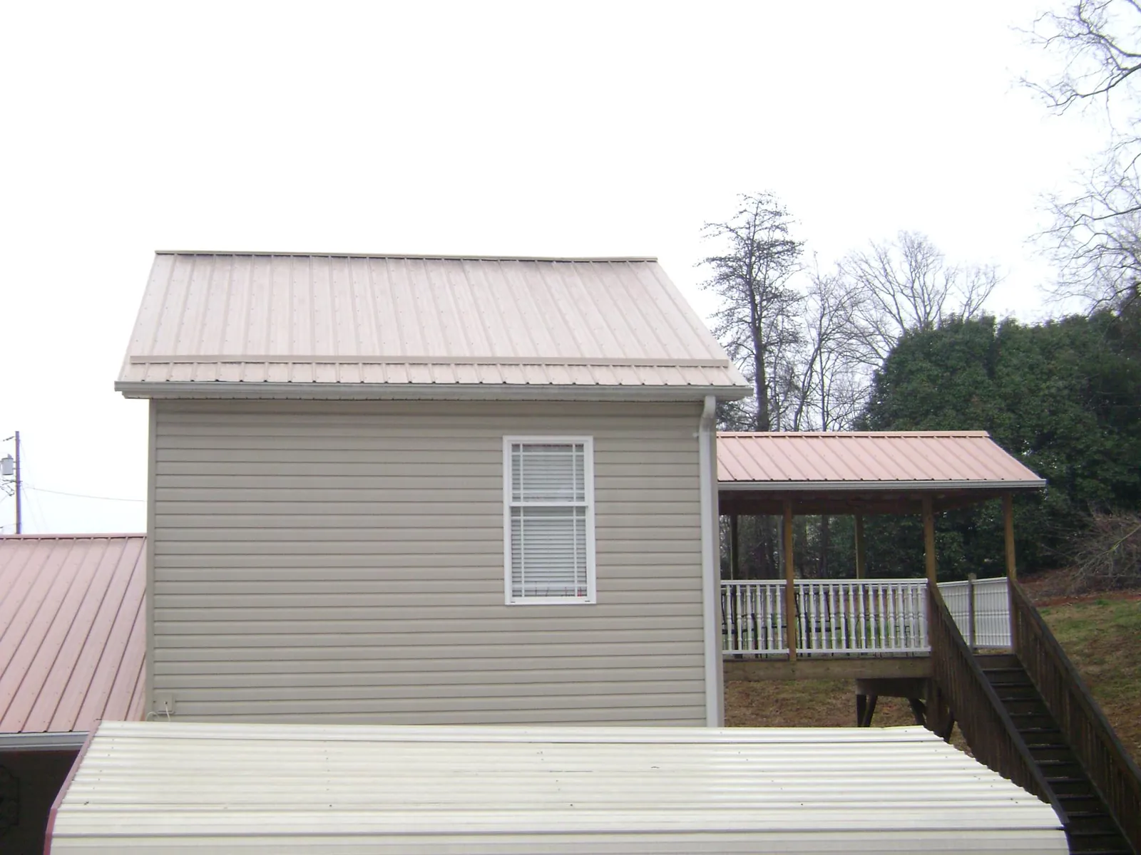 Tan metal roofs on a two story addition and attached porch, from a Roof Replacement job in Marlboro